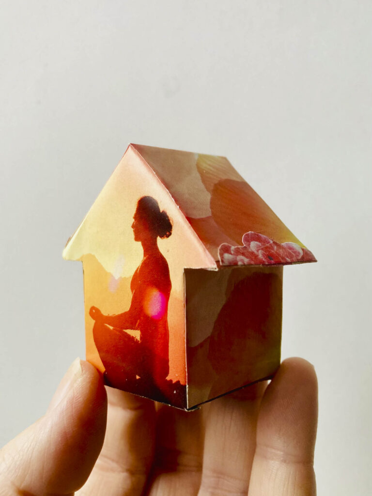 klein huisje met warme kleuren en een mediterend persoon op de voorkant.